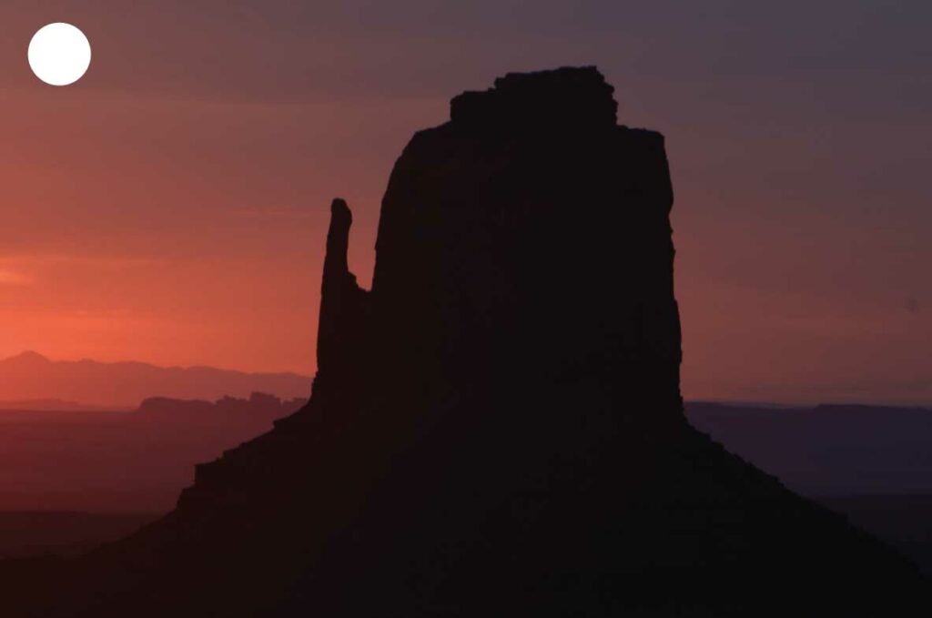 Mitaine de Monument Valley au lever du soleil, avec la lumière dorée illuminant les formations rocheuses emblématiques.