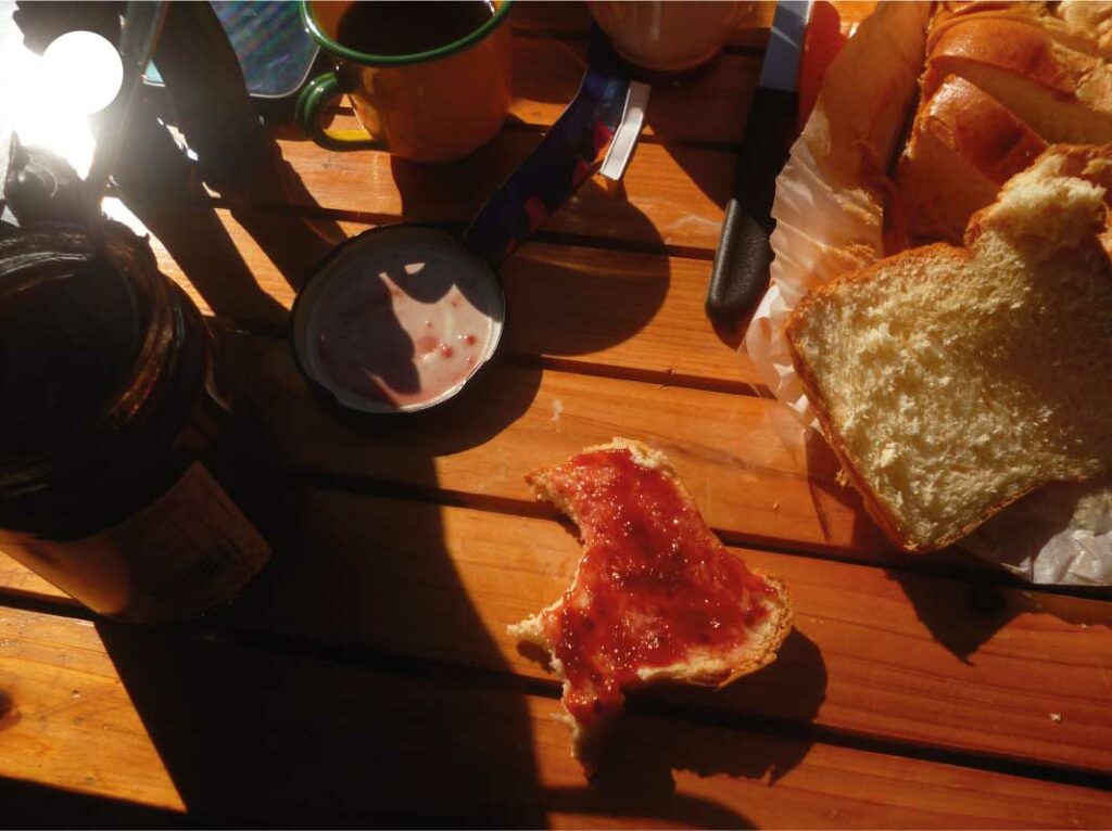 Gros plan sur une table en bois au petit déjeuner, avec biscotte et confiture à moitié entamée, illustrant un moment simple et authentique.