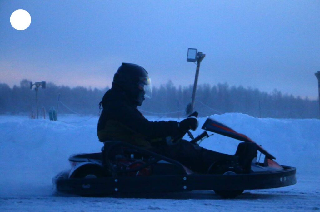 Kart sur glace en Laponie avec pilote casqué en pleine action, capturant la vitesse et l’intensité de la conduite sur circuit hivernal.