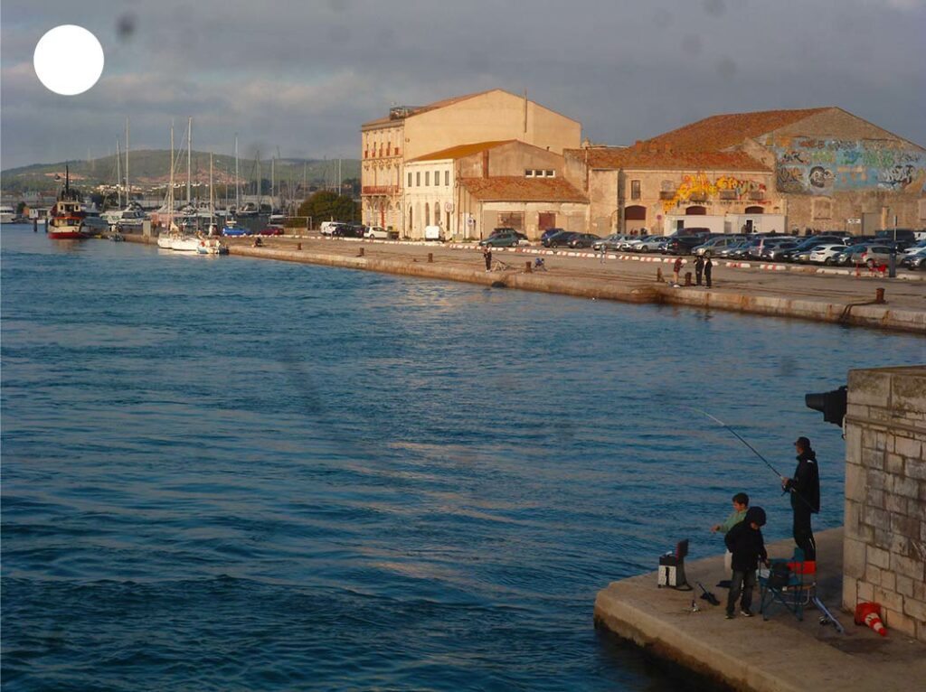 Quai au bord de l’eau à Sète avec des pêcheurs en activité et les bâtiments baignés par le soleil en arrière-plan, illustrant l’authenticité du port méditerranéen.