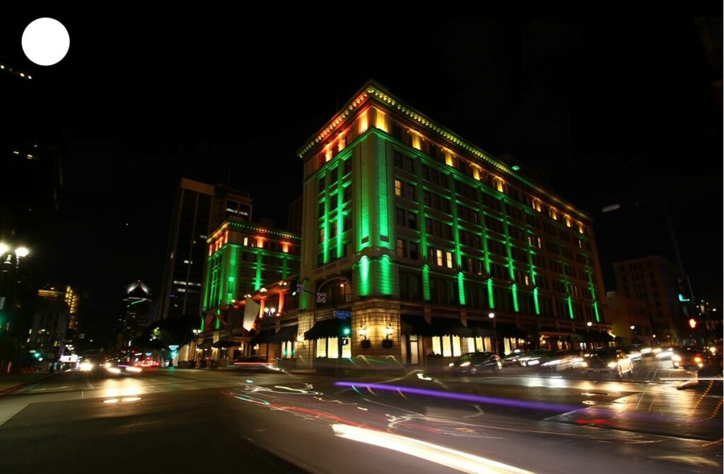 Bâtiment aux escaliers vert et jaune photographié de nuit, avec les lumières des voitures traçant des lignes dynamiques le long de la route.