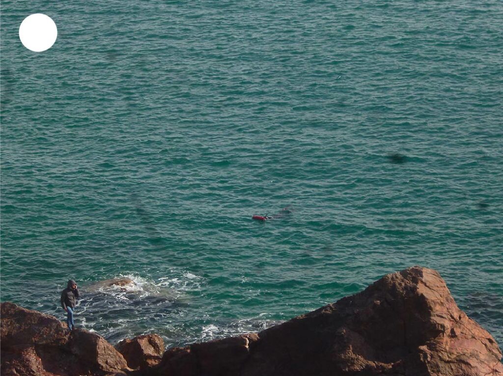 Rocher au bord de l’eau à Sète avec une personne marchant le long du rivage, entre mer et pierre sous une lumière naturelle.