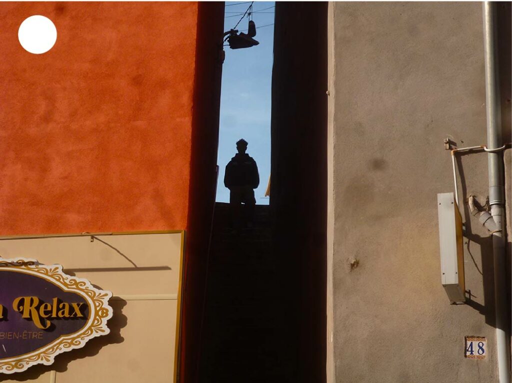 Ombre graphique entre deux bâtiments en haut d’un escalier à Sète, créant un jeu de lumière et de contraste architectural.